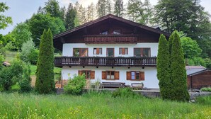 A two-story chalet with a balcony, surrounded by lush greenery and tall trees. - Ferienwohnung 2 Personen, 50 qm, - Hoher Göll, Sep. Schlafzimmer, Balkon (Schönau am Königssee)
