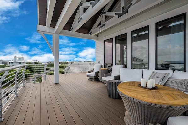 Um deck coberto ao ar livre com piso de madeira, móveis de vime e amplas janelas que oferecem vistas da região.