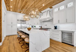 Uma cozinha moderna com armários brancos, uma ilha de mármore, piso de madeira e luminárias pendentes.