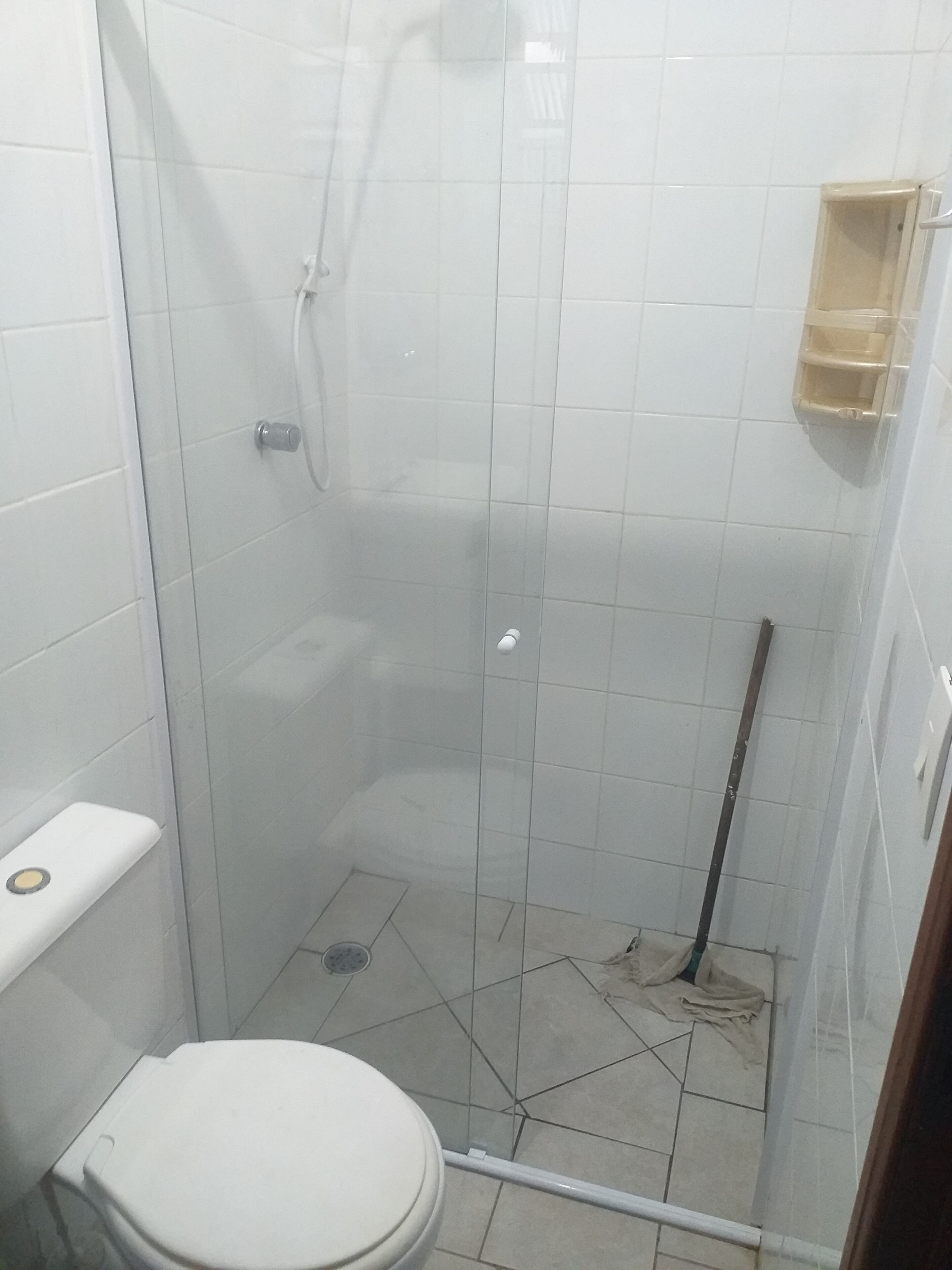 A small, tiled bathroom with a toilet, a shower enclosure, and a mop leaning against the wall.
