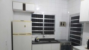 A kitchen with white cabinets, a built-in oven, a sink, and a window with blinds. - House with pool and barbecue in Caraguatatuba, in a gated community with Wi-Fi. (SP)