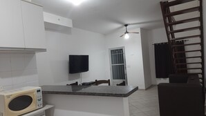 A kitchen with white cabinets, a microwave, a flat-screen TV, and a staircase. - House with pool and barbecue in Caraguatatuba, in a gated community with Wi-Fi. (SP)