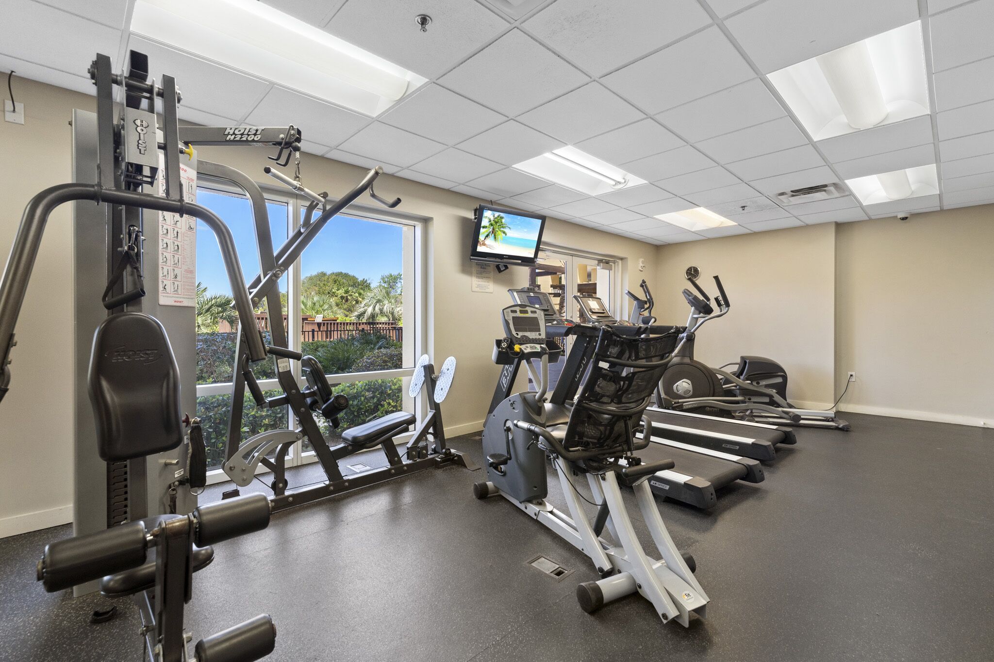 A gym with cardio machines, weight machines, and a TV screen.