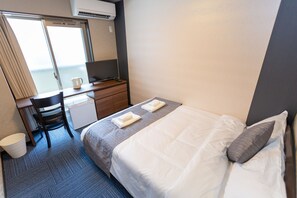 Una habitación de hotel con cama, escritorio, silla, una mesita y ventana.