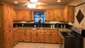 A kitchen with wooden cabinets, a granite countertop, a stove, and a window with a view of the outdoors.