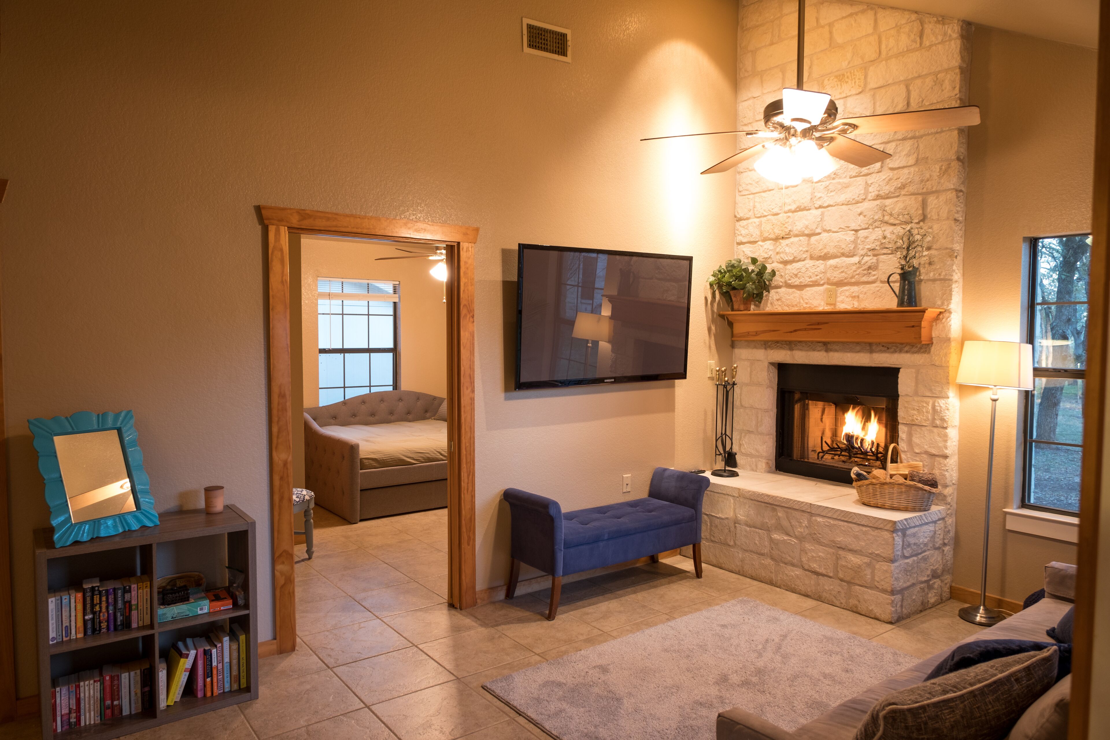 A cozy living room with a fireplace, a television mounted on the wall, and a bookshelf.