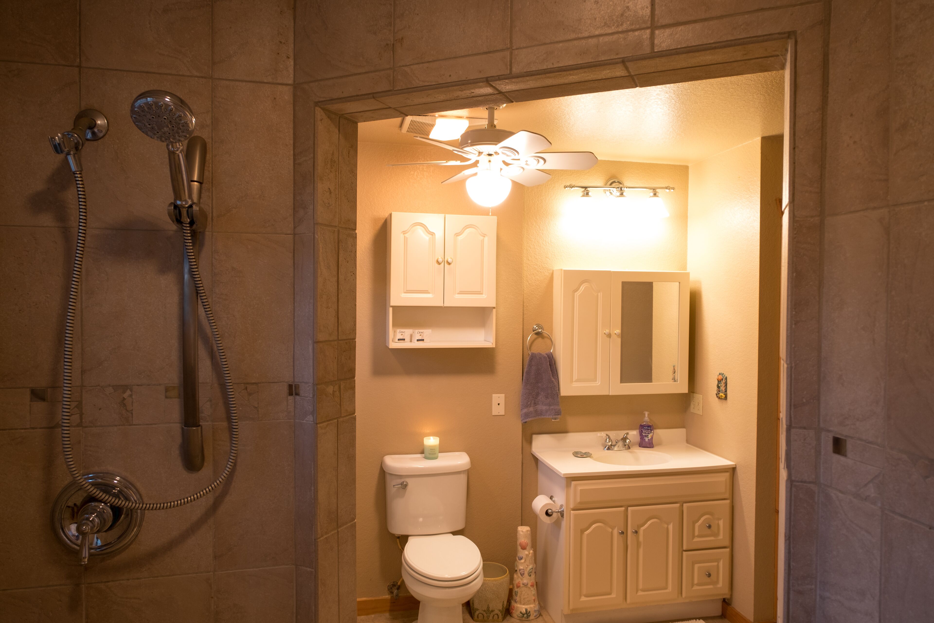 A bathroom with a shower, toilet, sink, and cabinets.