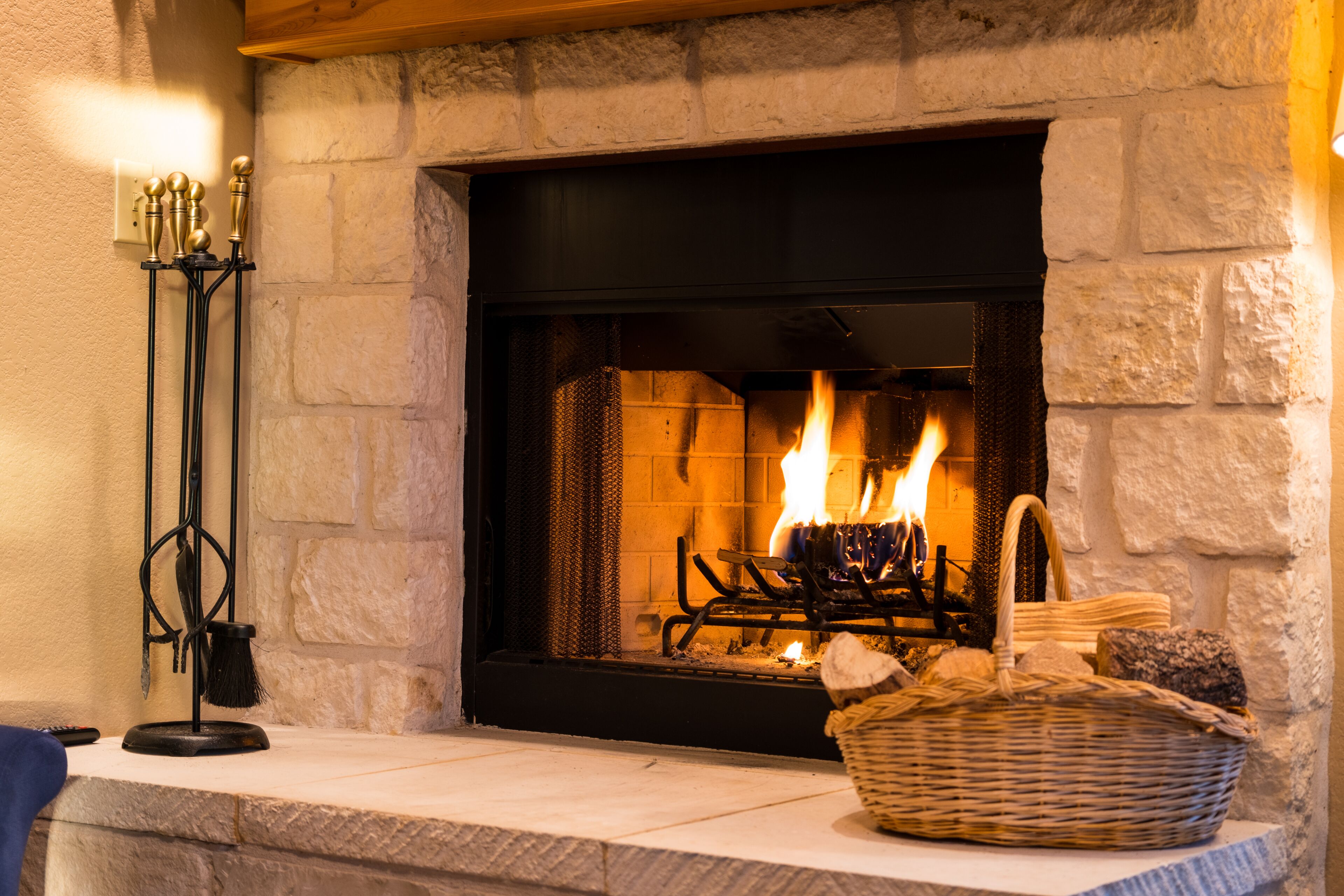 A fireplace with a stone surround, a basket of firewood, and a candle holder.