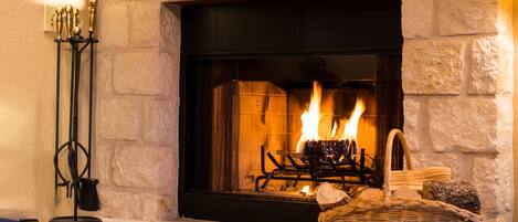 A fireplace with a stone surround, a basket of firewood, and a candle holder.