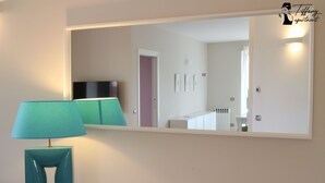 Une chambre moderne avec une lampe turquoise posée sur une table blanche, un grand miroir reflétant une porte et un meuble blanc.