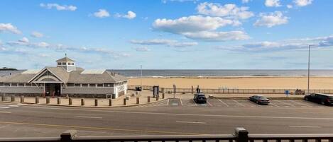 Une route côtière avec vue sur la plage, un bâtiment doté d’une tour et un parking rempli de voitures.