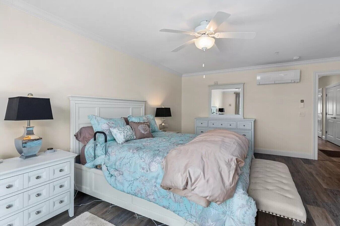 A bedroom with a bed, bedside tables, a ceiling fan, a mirror, and a door.