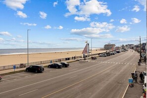 A beachside road with parked cars, a flag, and buildings including a hotel.