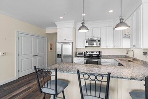 A kitchen with white cabinets, stainless steel appliances, granite countertops, and pendant lighting.