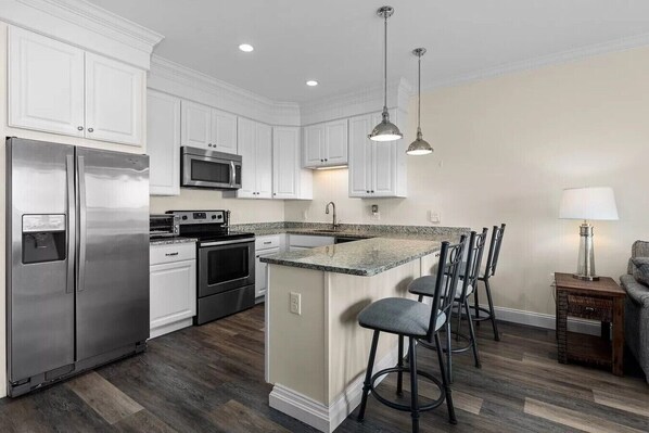 A kitchen with white cabinets, stainless steel appliances, a granite countertop, and a bar area with stools.