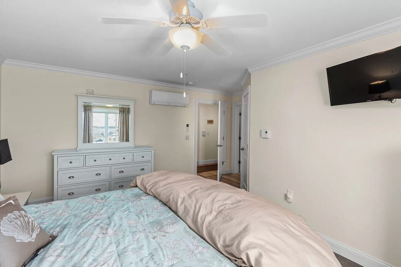 Une chambre à coucher comprenant un lit, une commode, un ventilateur de plafond et un téléviseur fixé au mur.