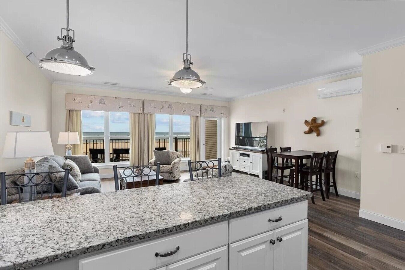 Een moderne keuken met granieten aanrechtbladen, een eethoek met een tafel en stoelen, en uitzicht op het strand door grote ramen.