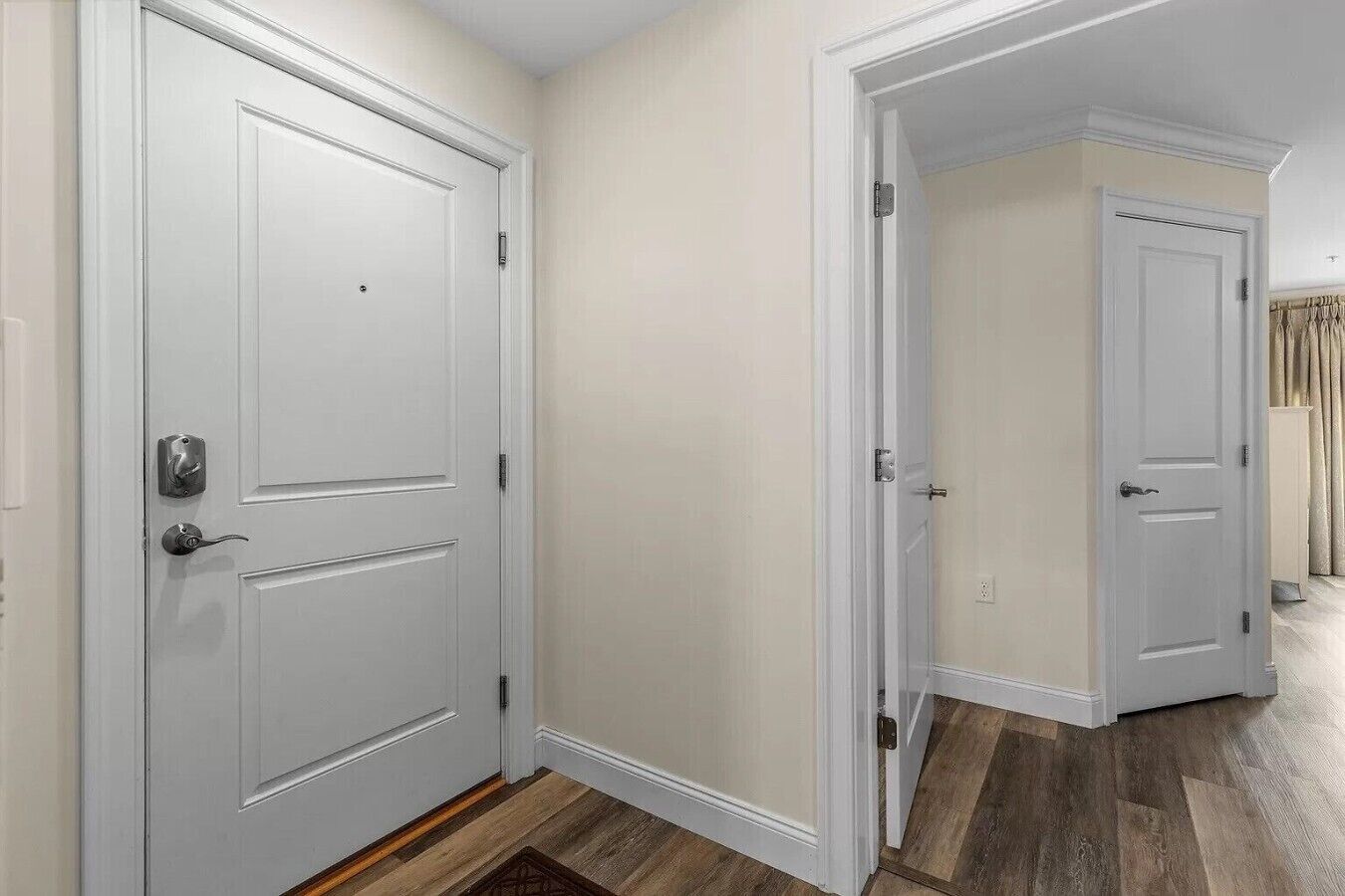A hallway with two white doors, wooden flooring, and a plain wall.