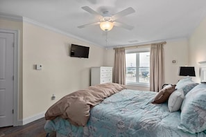 A bedroom with a bed, a ceiling fan, a TV, and a window with curtains.