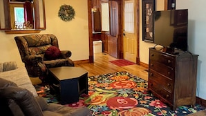 Una sala de estar con un sofá, una silla, una mesita de centro, un televisor, una chimenea y piso de madera.
