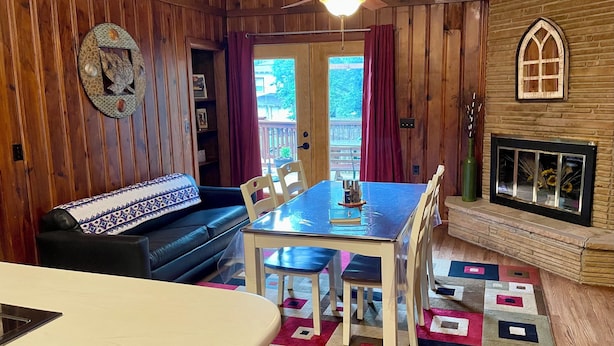 Una habitación acogedora con paredes de madera, una mesa de comedor con sillas, un sofá, un ventilador de techo y una chimenea.