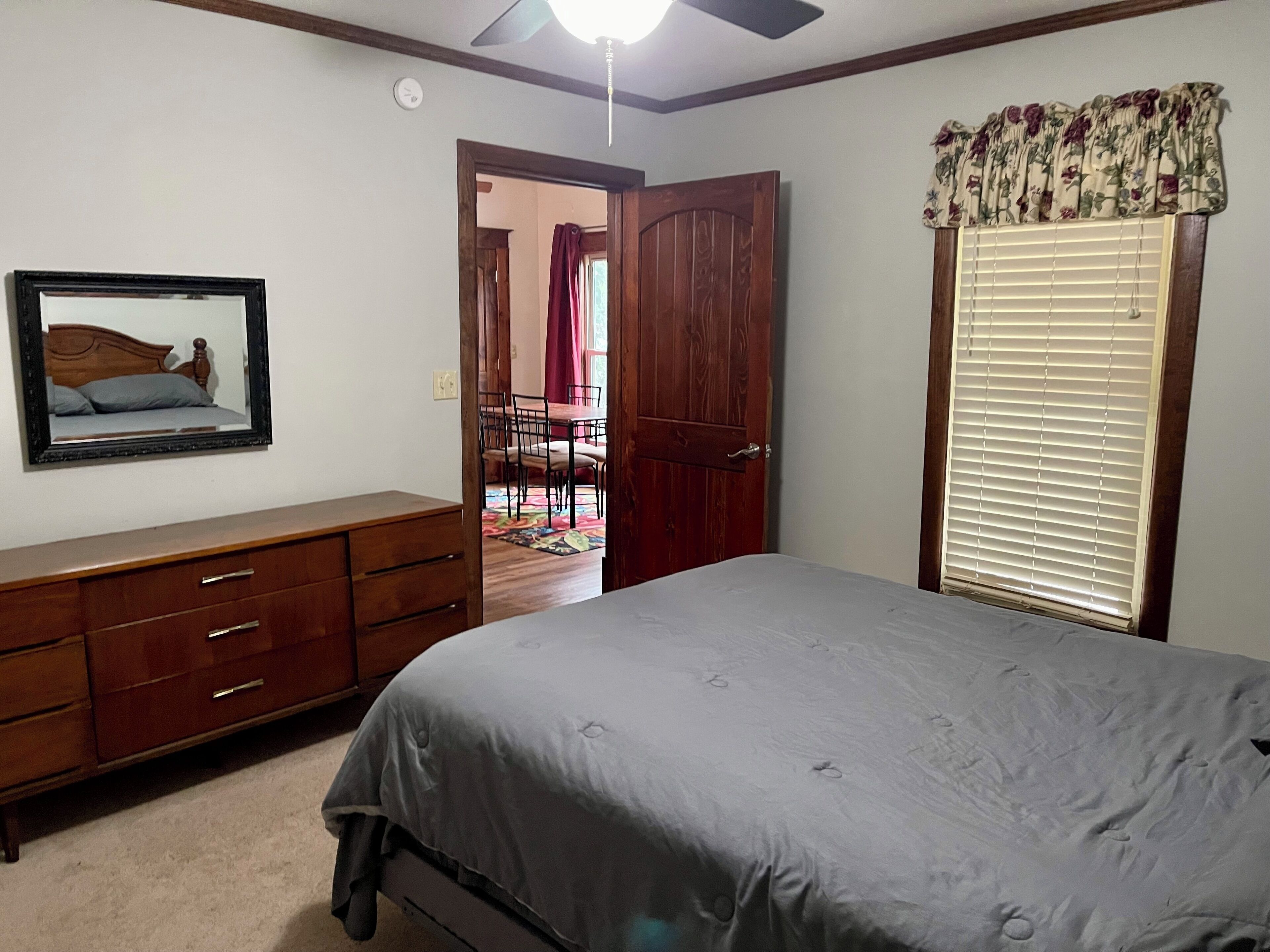 A bedroom with a bed, a dresser, a mirror, a door, and a window with blinds.