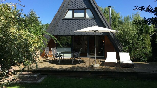 A modern house with a triangular roof, a patio with outdoor furniture, and a large umbrella. - Cottage with fireplace, near the beach, dogs welcome, kitchen is new, fenced  (Damp)