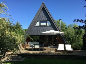 A modern house with a triangular roof, a patio with outdoor furniture, and a large umbrella. - Cottage with fireplace, near the beach, dogs welcome, kitchen is new, fenced (Damp)