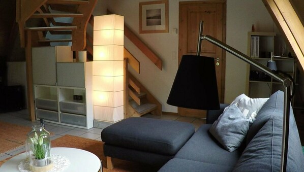A living room with a sofa, a lamp, and a glass bottle with a plant. - Cottage with fireplace, near the beach, dogs welcome, kitchen is new, fenced (Damp)