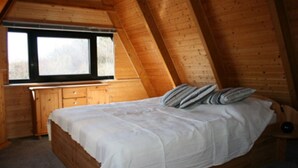 A wooden cabin bedroom with a bed, a window, and a wooden dresser. - Cottage with fireplace, near the beach, dogs welcome, kitchen is new, fenced  (Damp)