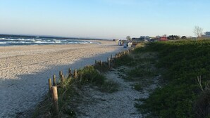 A sandy beach with a wooden fence and a path leading to a building in the distance. - Cottage with fireplace, near the beach, dogs welcome, kitchen is new, fenced  (Damp)
