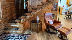 L’intérieur d’un chalet rustique, avec un escalier en bois, un fauteuil inclinable en cuir et un coin cuisine.