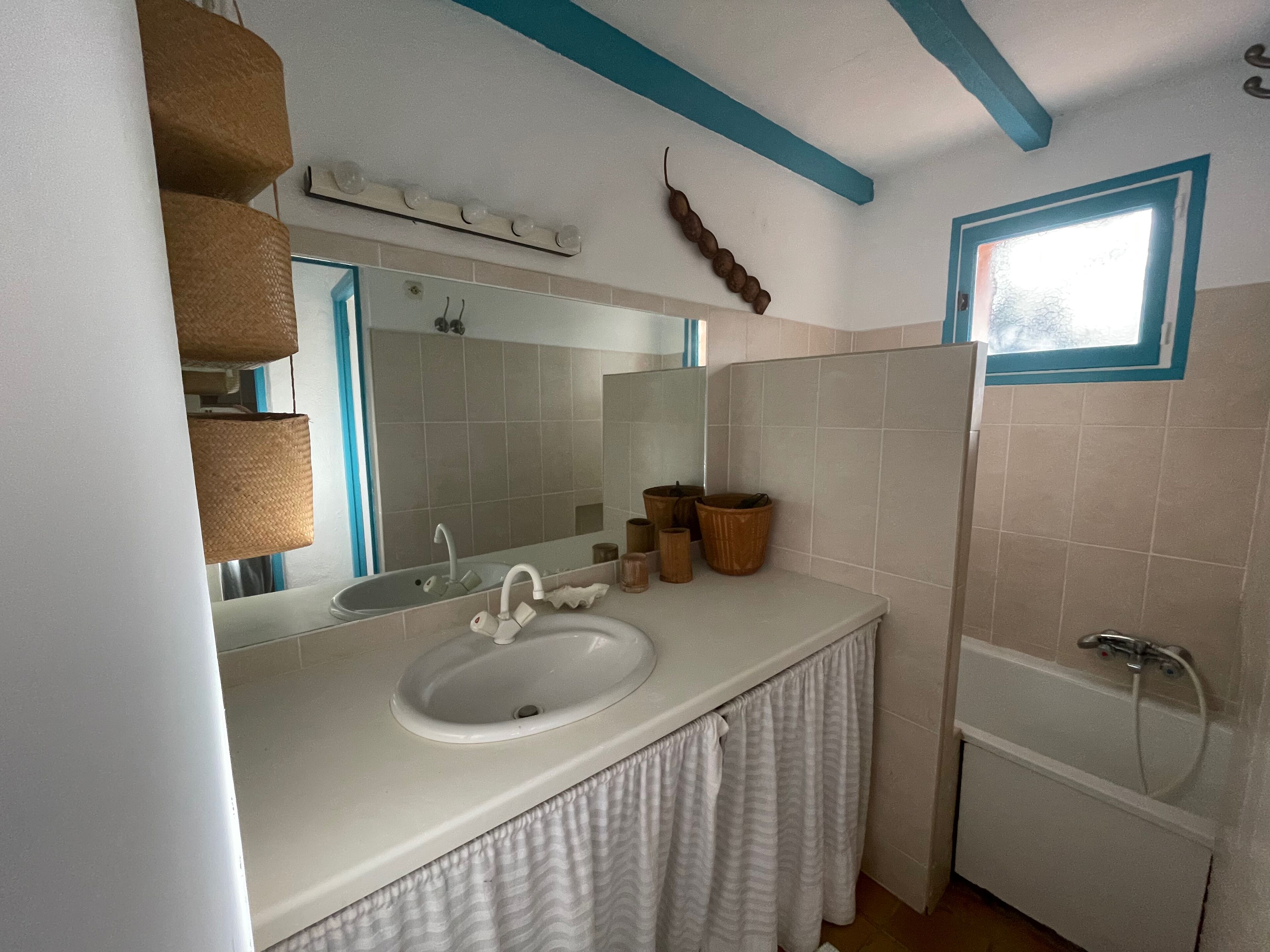 A bathroom with a white sink, a mirror, a bathtub, and a window.