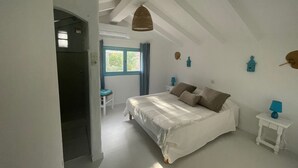 Een slaapkamer met een bed, een raam, een stoel en een kleine tafel met een lamp.