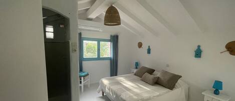 Een slaapkamer met een bed, een raam, een stoel en een kleine tafel met een lamp.