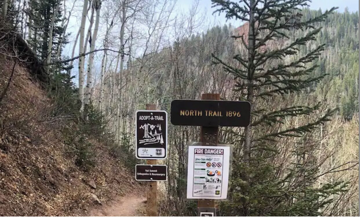 Ein Wegweiser mit der Aufschrift 'NORTH TRAIL 1896' und Informationen zum Programm 'ADOPT-A-TRAIL'.