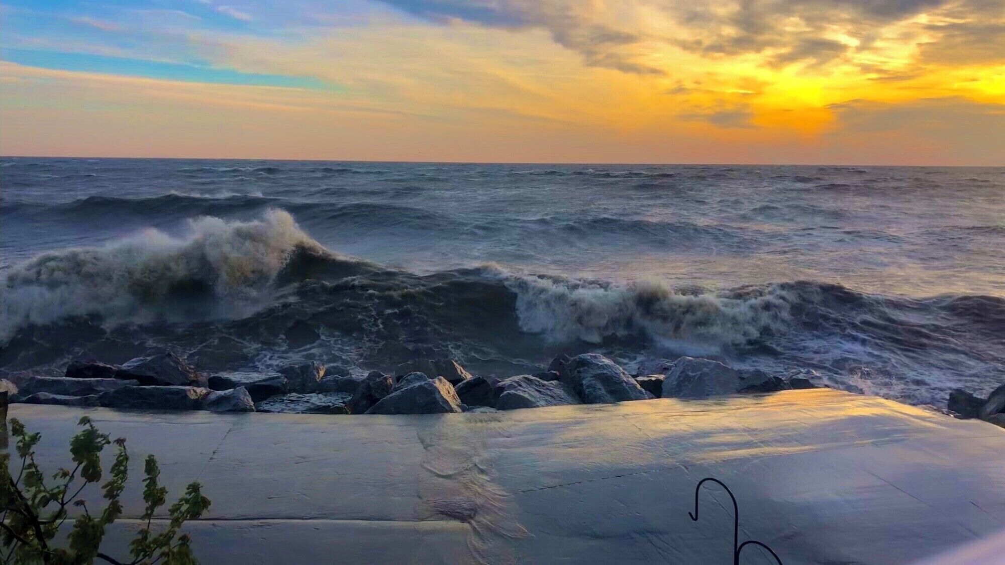 Una playa con olas rompiendo sobre rocas y un atardecer al fondo.