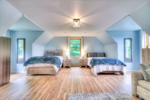 Une chambre avec deux lits, un plancher en bois, une grande fenêtre et un luminaire au plafond.
