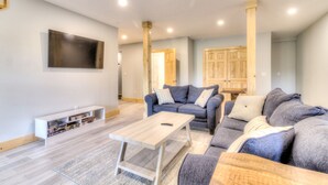 A modern living room with a grey sofa, a wooden coffee table, and a TV mounted on the wall.