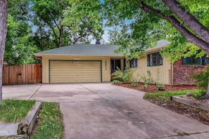 A single-story house with a garage, a brick section, and a wooden fence. - Charming Five Bedroom Denver Home | The Pink Palace (Denver)