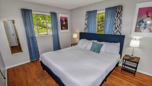Un dormitorio con una cama grande, dos mesitas de noche con lámparas, un espejo y cortinas en dos ventanas.