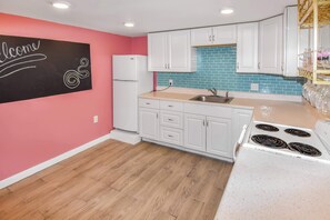Una cocina con armarios blancos, un refrigerador blanco, un lavamanos y una estufa.