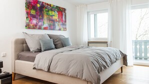 A modern bedroom with a bed, a colorful abstract painting, and a view of the outdoors. - Fantastisch im Naturpark Altmühltal (Greding)