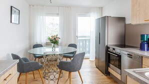 A compact kitchen with a refrigerator, oven, and dishwasher. There is a round glass table with four chairs and a vase of flowers. - Fantastisch im Naturpark Altmühltal (Greding)
