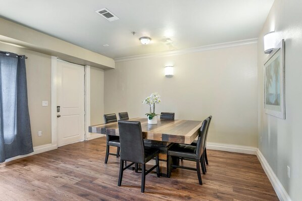 Un coin repas avec une table en bois et six chaises, une petite plante en pot et un luminaire fixé au mur.
