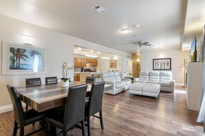 Un vaste salon comprenant un coin repas, une cuisine à l’arrière-plan et un ventilateur de plafond.