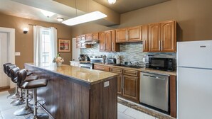 A modern kitchen with wooden cabinets, a granite countertop, stainless steel appliances, and a bar area with stools. - 20% OFF Monthly | 10% OFF Weekly-St. Charles Ave Condo – Minutes to FQ (New Orleans)