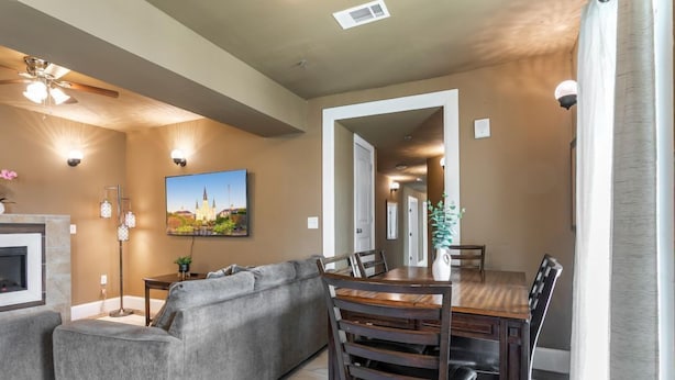 A living room with a gray sectional sofa, a wooden dining table with chairs, a fireplace, and a ceiling fan. - 20% OFF Monthly | 10% OFF Weekly-St. Charles Ave Condo – Minutes to FQ (New Orleans)