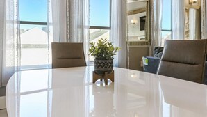 A hotel room with a large round table, two chairs, a potted plant, and a large window with curtains.