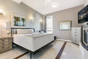 Un dormitorio moderno con una cama grande, una mesita de noche, un aparador, un televisor y un cuadro de palmeras.